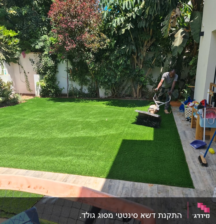 אדם משתמש במכונת דשא על דשא סינתטי בגינה